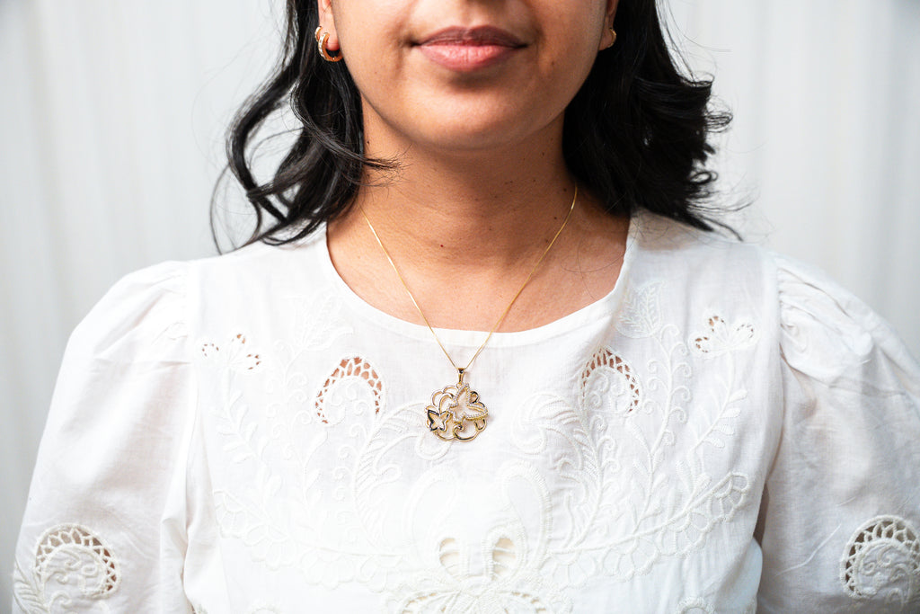 Woman wearing a white embroidered top with a necklace against a light background