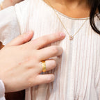 Person wearing a gold necklace with a small pendant, held by another person. Harma_Jewelry_Gold_Plated_Little_Bloom_PINK_Zirconia_Necklace_2