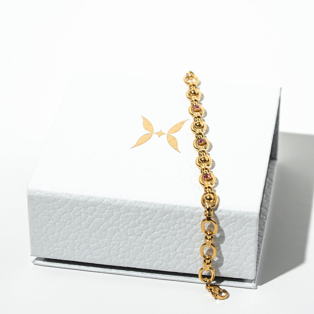 Gold bracelet with red stones on a white surface. Harma Jewelry Gold plated Unbreakable Link Pink Zirconia Bracelet