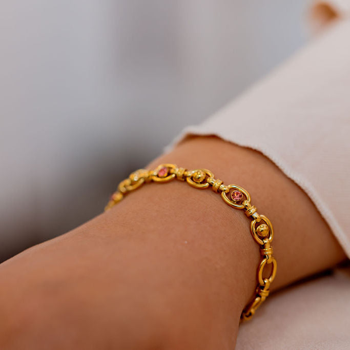 Gold bracelet on a wrist with a blurred background. Harma Jewelry Gold plated Unbreakable Link Pink Zirconia Bracelet