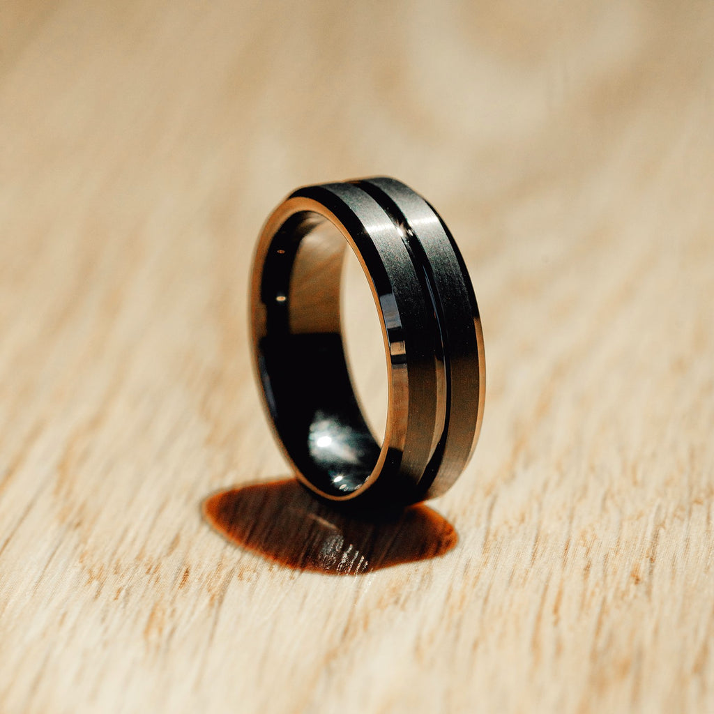 Black and gold ring on a wooden surface Harma Jewelry Men Tungsten Carbide Band Ring Black Barrel Simple