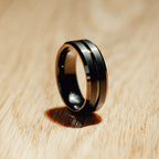 Black and gold ring on a wooden surface Harma Jewelry Men Tungsten Carbide Band Ring Black Barrel Simple