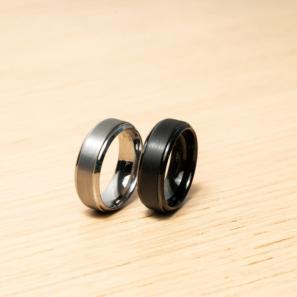 Two rings, one silver and one black, on a wooden surface Harma Jewelry Men Tungsten Carbide Band Ring Black Silver Simple 