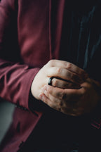 Close-up of a person's hands with a dark ring, wearing a burgundy sleeve. Harma Jewelry Men Tungsten Carbide Band Ring Black Simple 