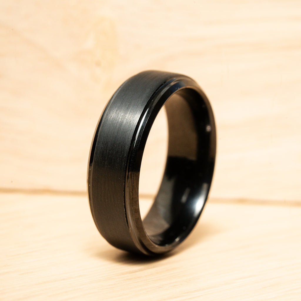Black ring on a wooden surface. Harma Jewelry Men Tungsten Carbide Band Ring Black Simple 