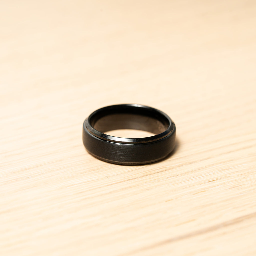 Black ring on a wooden surface. Harma Jewelry Men Tungsten Carbide Band Ring Black Silver Simple 