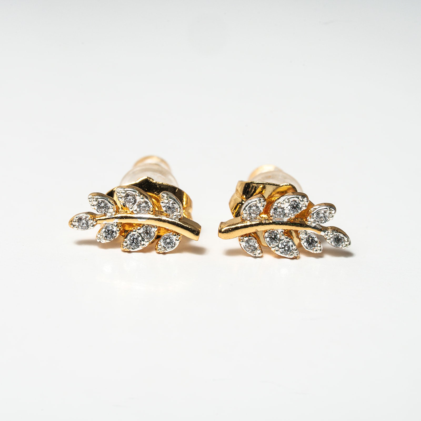 Gold leaf-shaped earrings with clear gemstones on a white background. Harma Jewelry Olive Branch Of Hope Stud Earrings Full Cubic Zirconia Gold Plated
