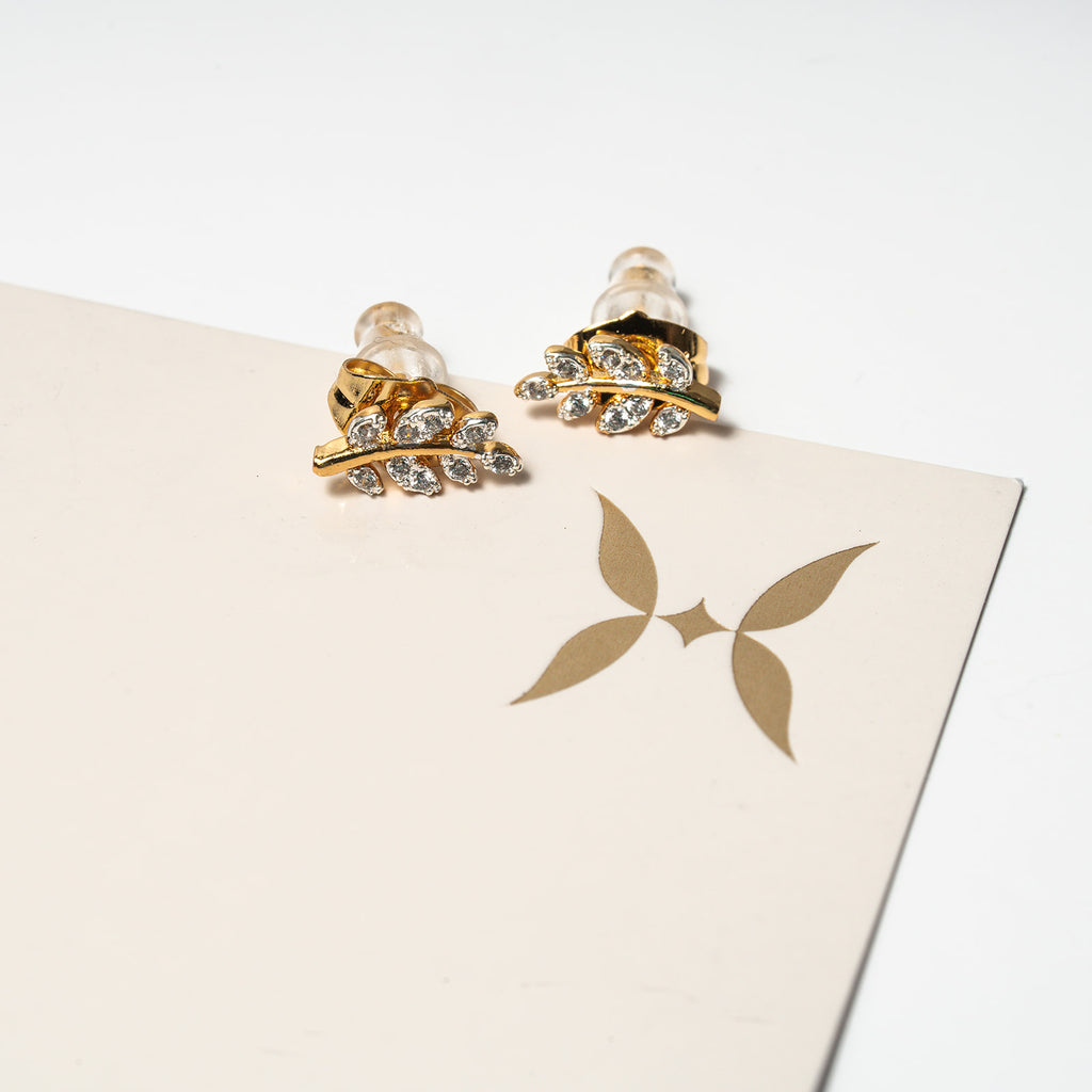 Gold and crystal earrings on a beige card with a logo. Harma Jewelry Olive Branch Of Hope Stud Earrings Full Cubic Zirconia Gold Plated