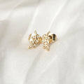 Gold leaf-shaped earrings with clear stones on a white fabric background