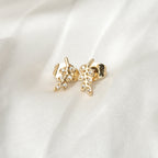 Gold leaf-shaped earrings with clear stones on a white fabric background