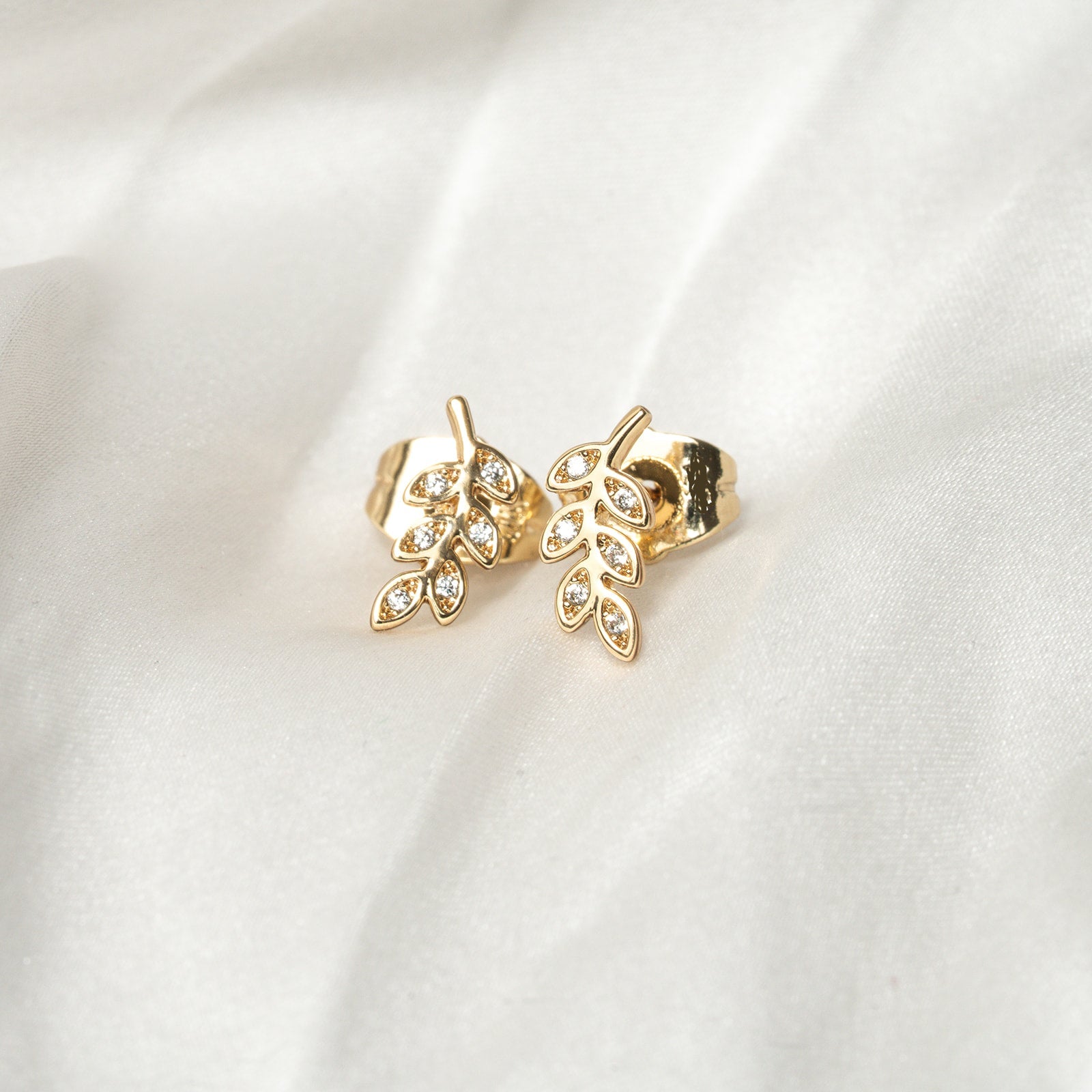 Gold leaf-shaped earrings with clear stones on a white fabric background