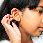 Close-up of a person wearing a gold earring, with a hand adjusting it.
