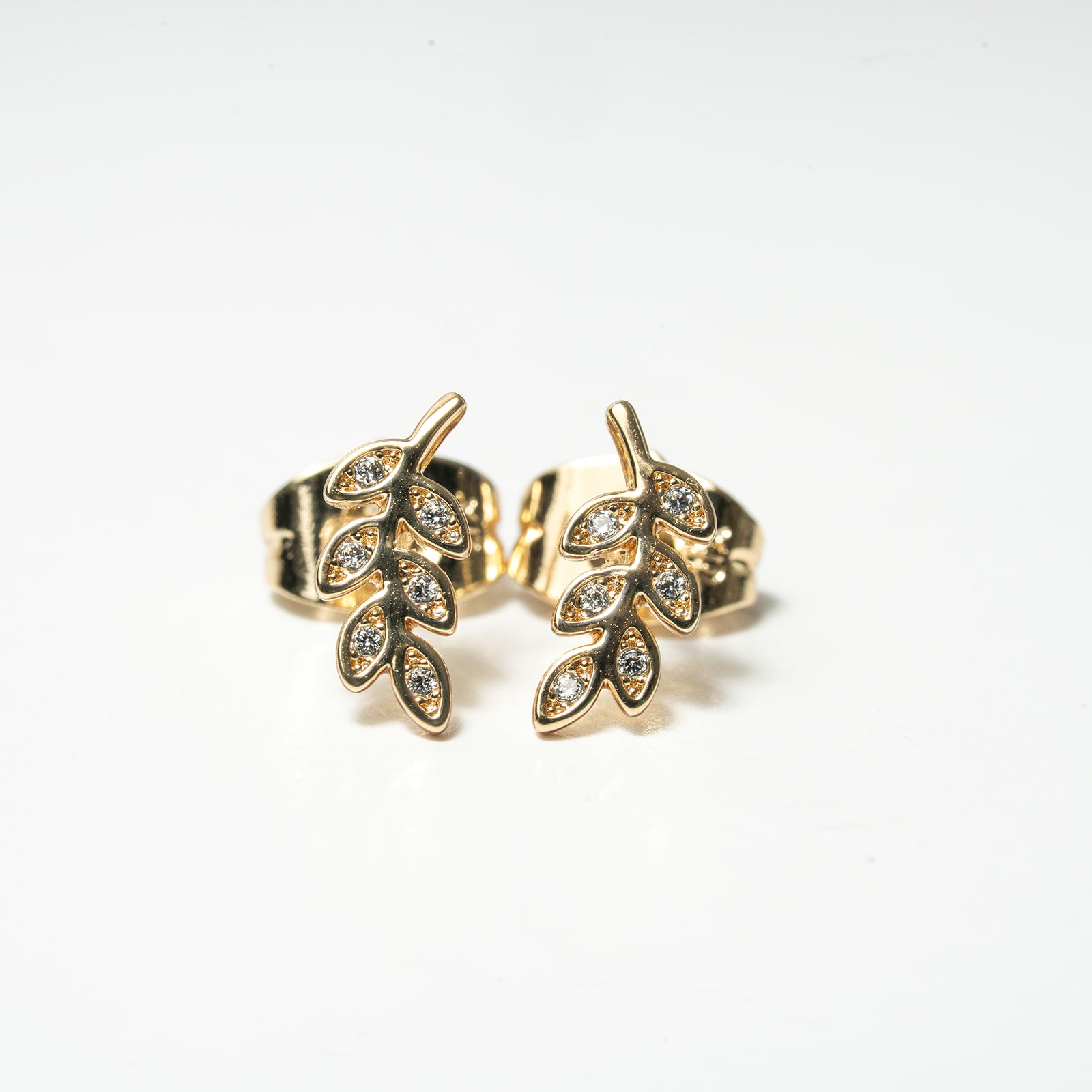 Gold leaf-shaped earrings with embedded stones on a white background