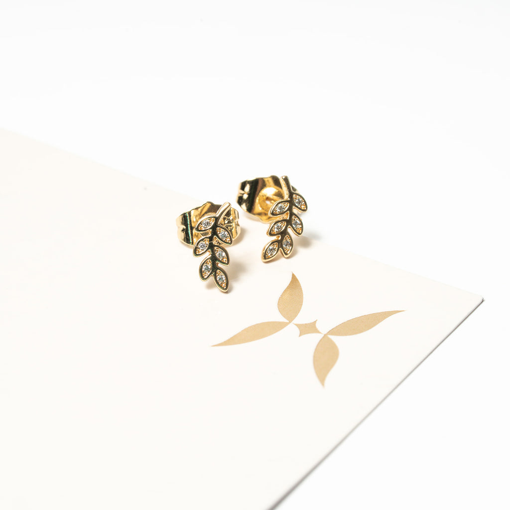 Gold leaf-shaped earrings on a white background with a brand logo.