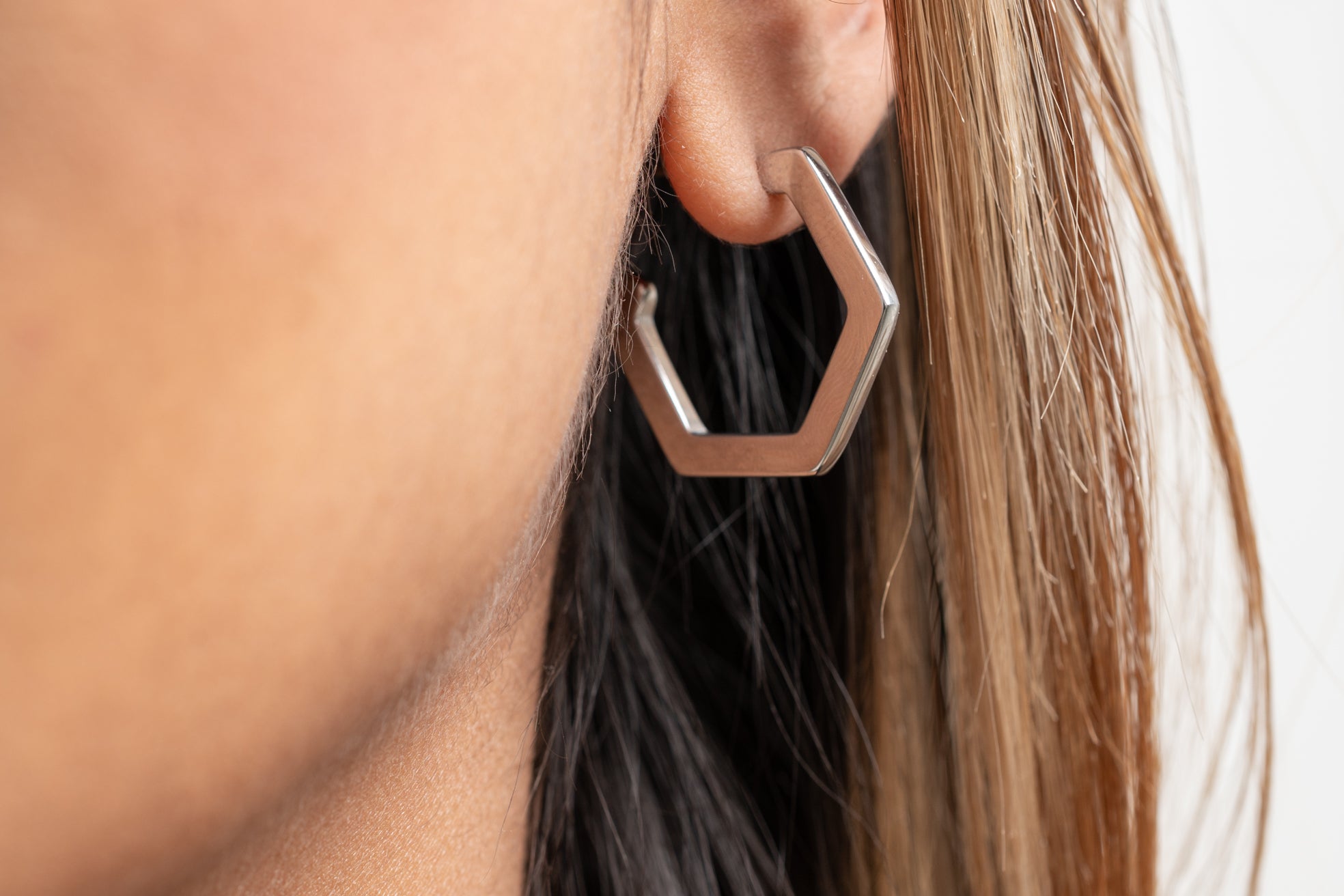 Close-up of a person wearing a hexagonal earring with a neutral background