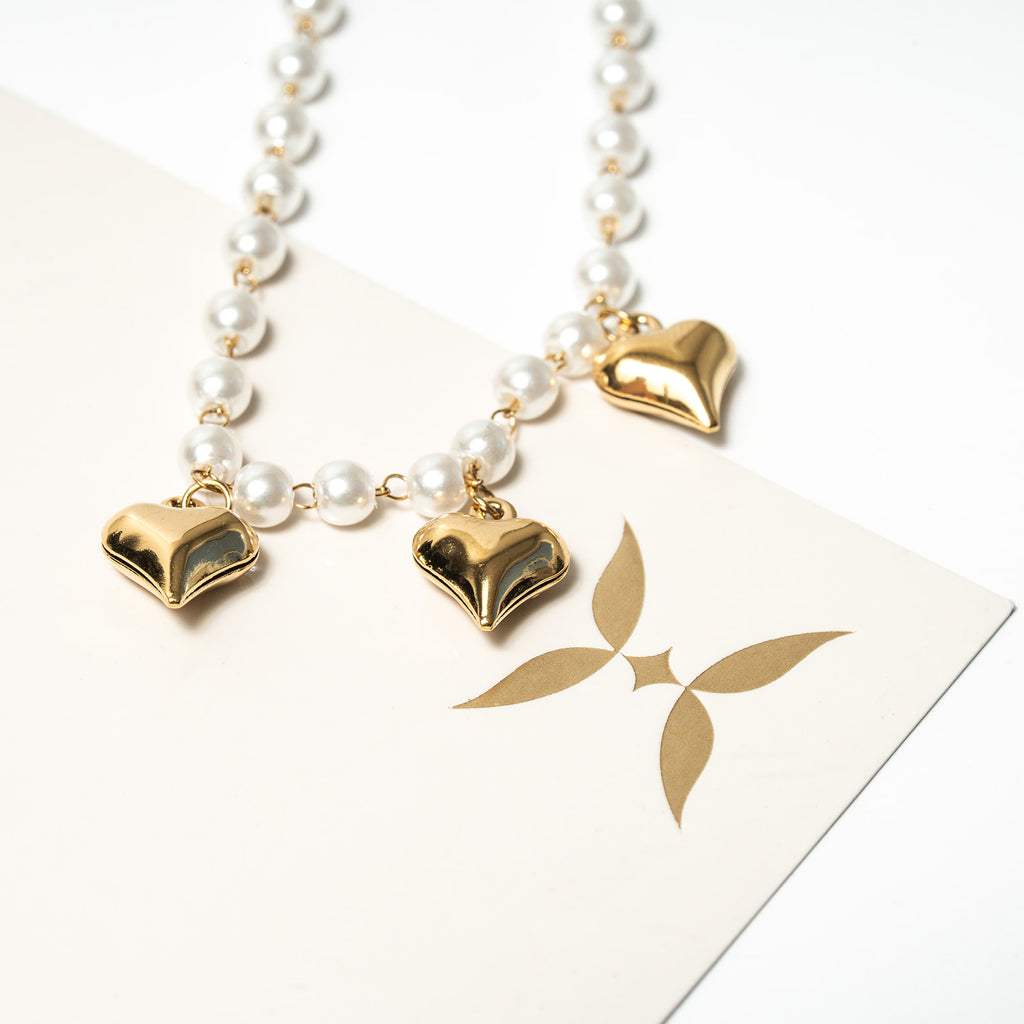 Necklace with heart-shaped gold pendants on a white background. Harma Jewelry White Pearl Gold Heart Charm Bracelet