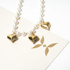 Necklace with heart-shaped gold pendants on a white background. Harma Jewelry White Pearl Gold Heart Charm Bracelet
