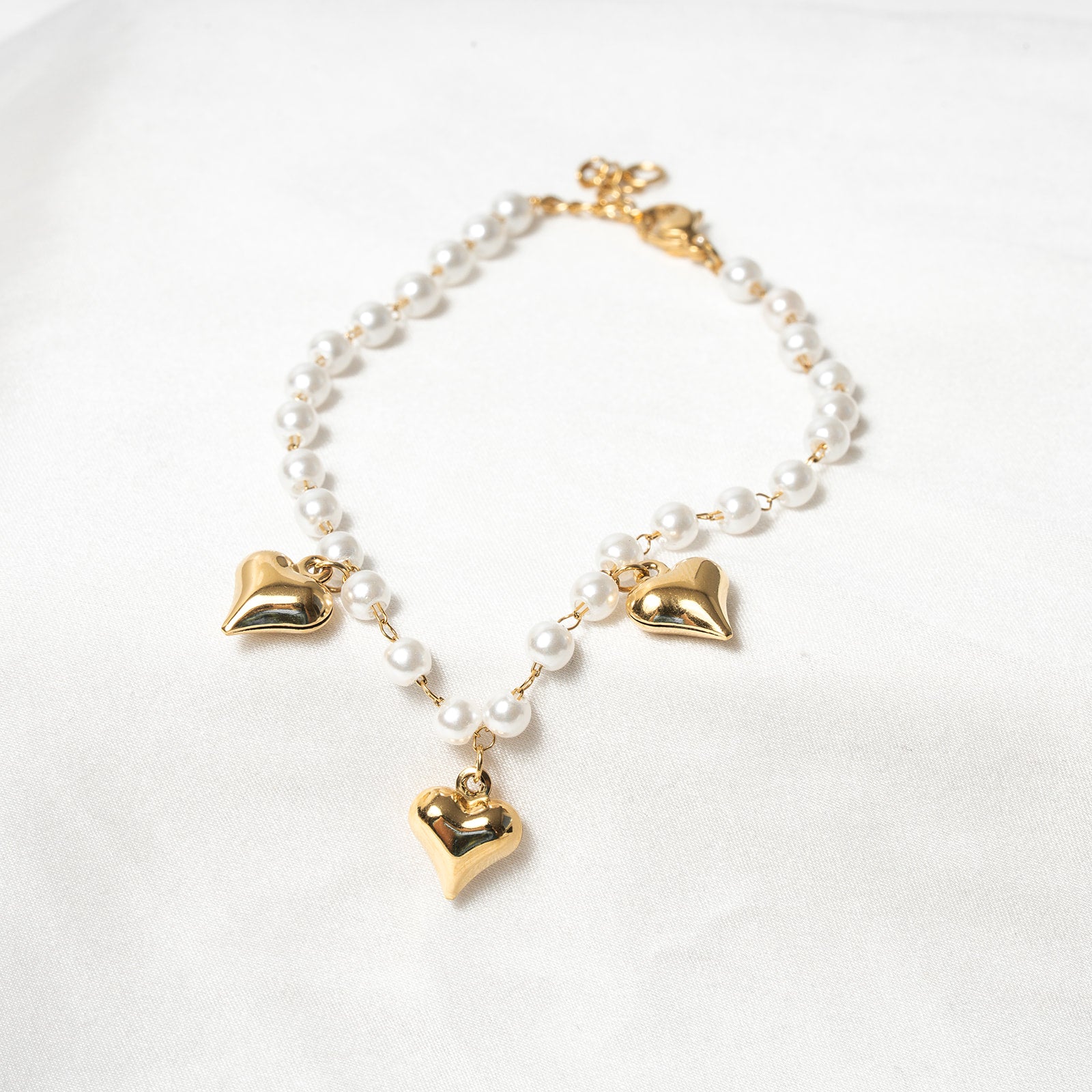 Bracelet with gold heart-shaped charms and white beads on a light background. Harma Jewelry White Pearl Gold Heart Charm Bracelet