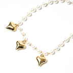 Pearl necklace with gold heart-shaped pendants on a white background. Harma Jewelry White Pearl Gold Heart Charm Bracelet