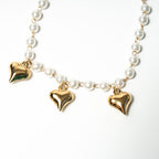 Pearl necklace with gold heart-shaped pendants on a white background. Harma Jewelry White Pearl Gold Heart Charm Bracelet