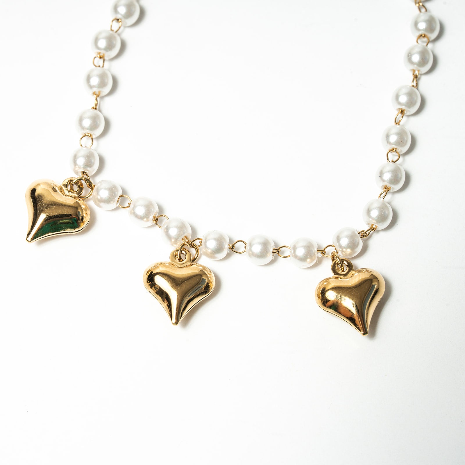 Pearl necklace with gold heart-shaped pendants on a white background. Harma Jewelry White Pearl Gold Heart Charm Bracelet