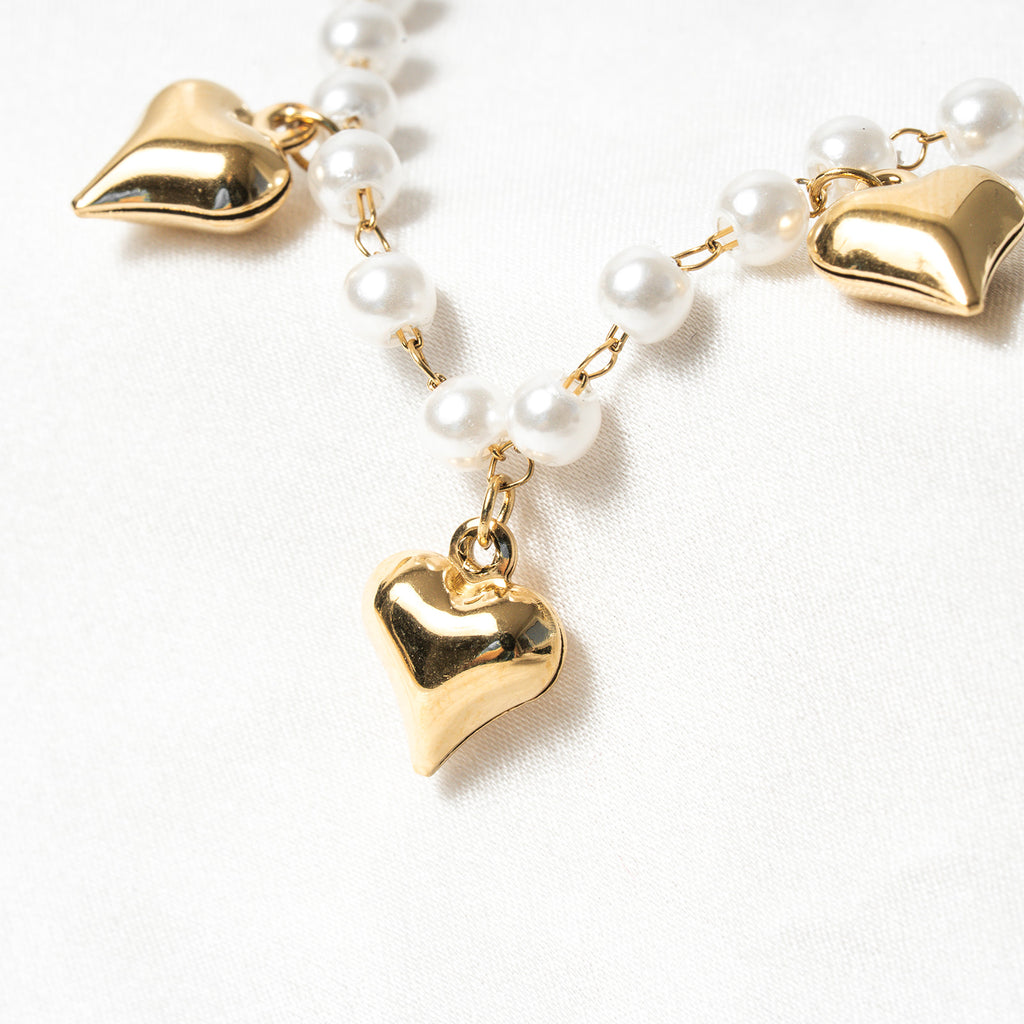 Pearl necklace with gold heart pendants on a white background. Harma Jewelry White Pearl Gold Heart Charm Bracelet