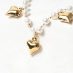 Pearl necklace with gold heart pendants on a white background. Harma Jewelry White Pearl Gold Heart Charm Bracelet