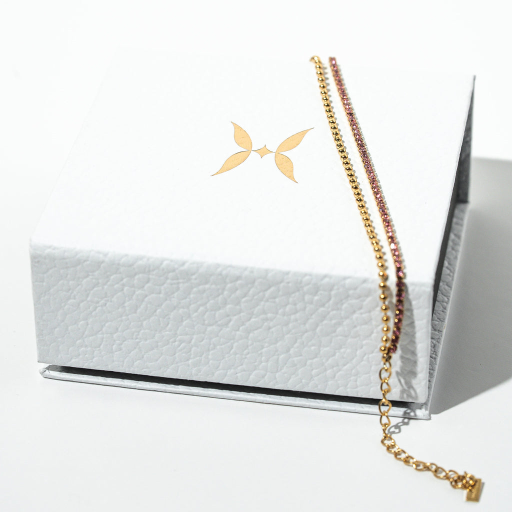 Gold chain necklace on a white textured box with a minimalistic design. Harma Jewelry gold plated Dual Radiance PINK Tennis Bracelet