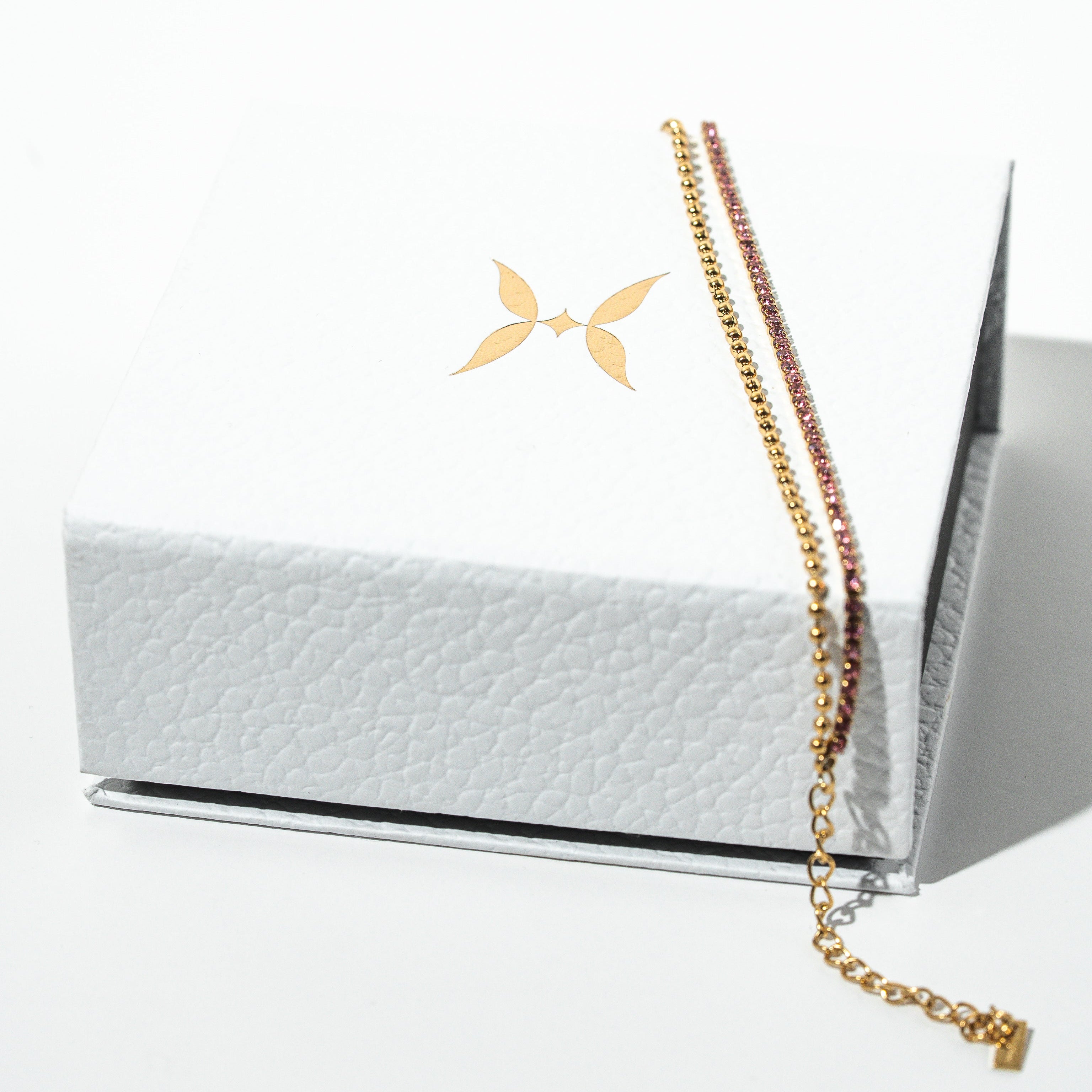 Gold chain necklace on a white textured box with a minimalistic design. Harma Jewelry gold plated Dual Radiance PINK Tennis Bracelet