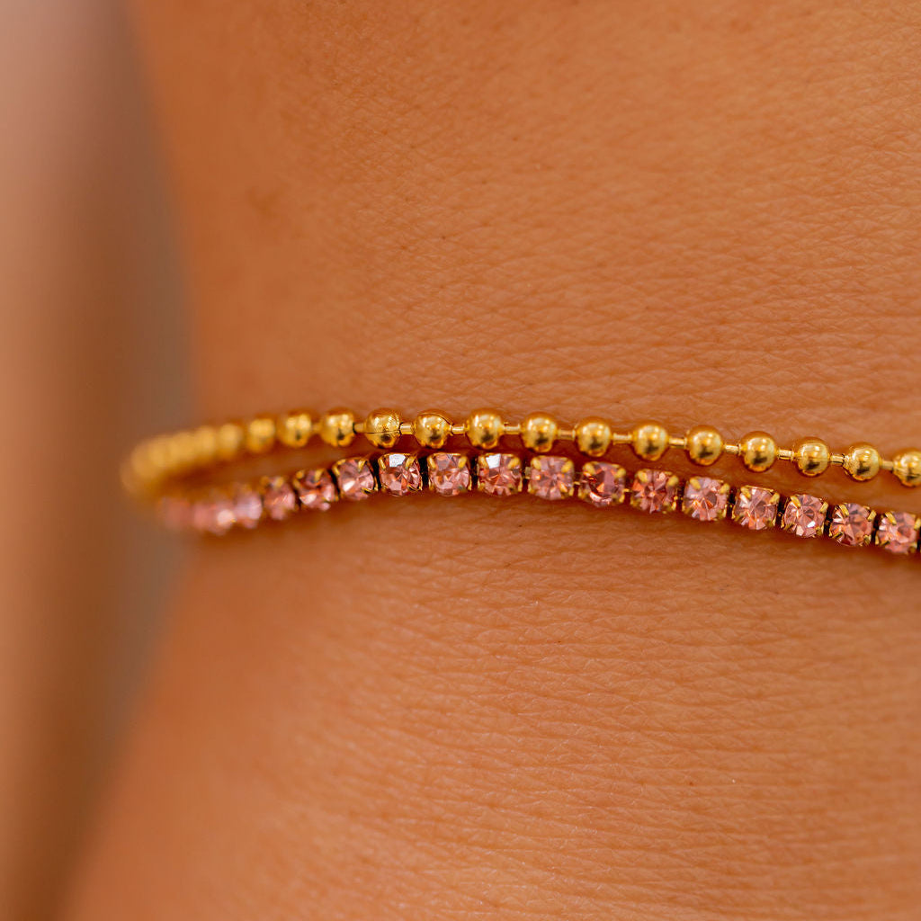 Close-up of a person wearing a gold bracelet with pink stones on a light brown background Harma Jewelry gold plated Dual Radiance PINK Tennis Bracelet