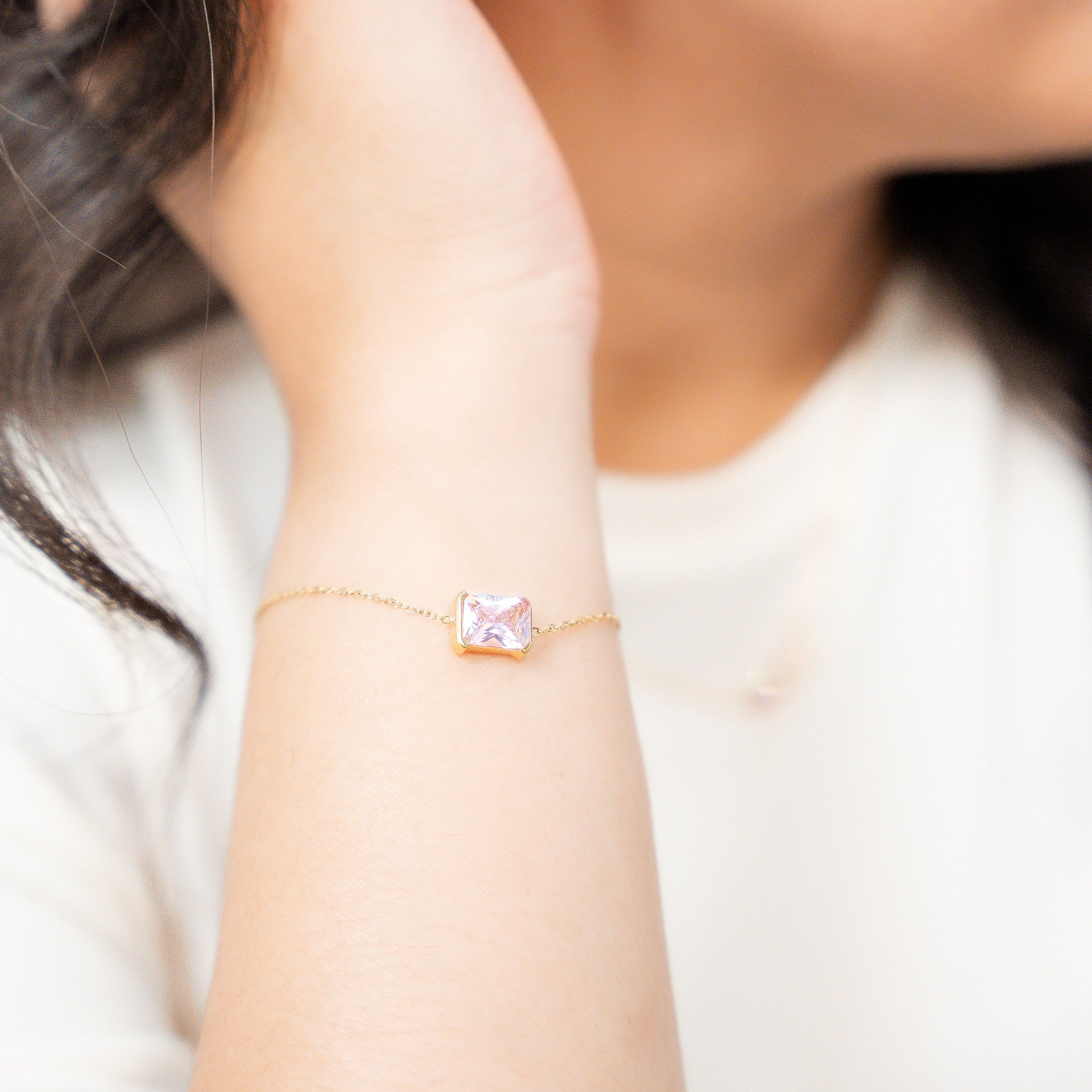 Close-up of a person wearing a gold bracelet with a pink gemstone and earrings. Harma Jewelry gold plated I Am Centered PINK Zirconia Bracelet