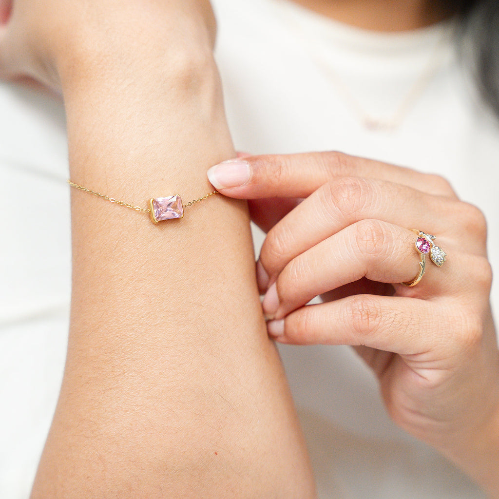 Close-up of a hand wearing a bracelet and ring, with another hand adjusting a bracelet on a wrist. Harma Jewelry gold plated I Am Centered PINK Zirconia Bracelet