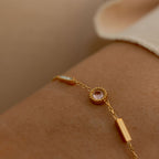 Gold bracelet with a pink gemstone on a wrist against a neutral background
