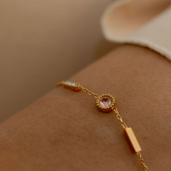 Gold bracelet with a pink gemstone on a wrist against a neutral background