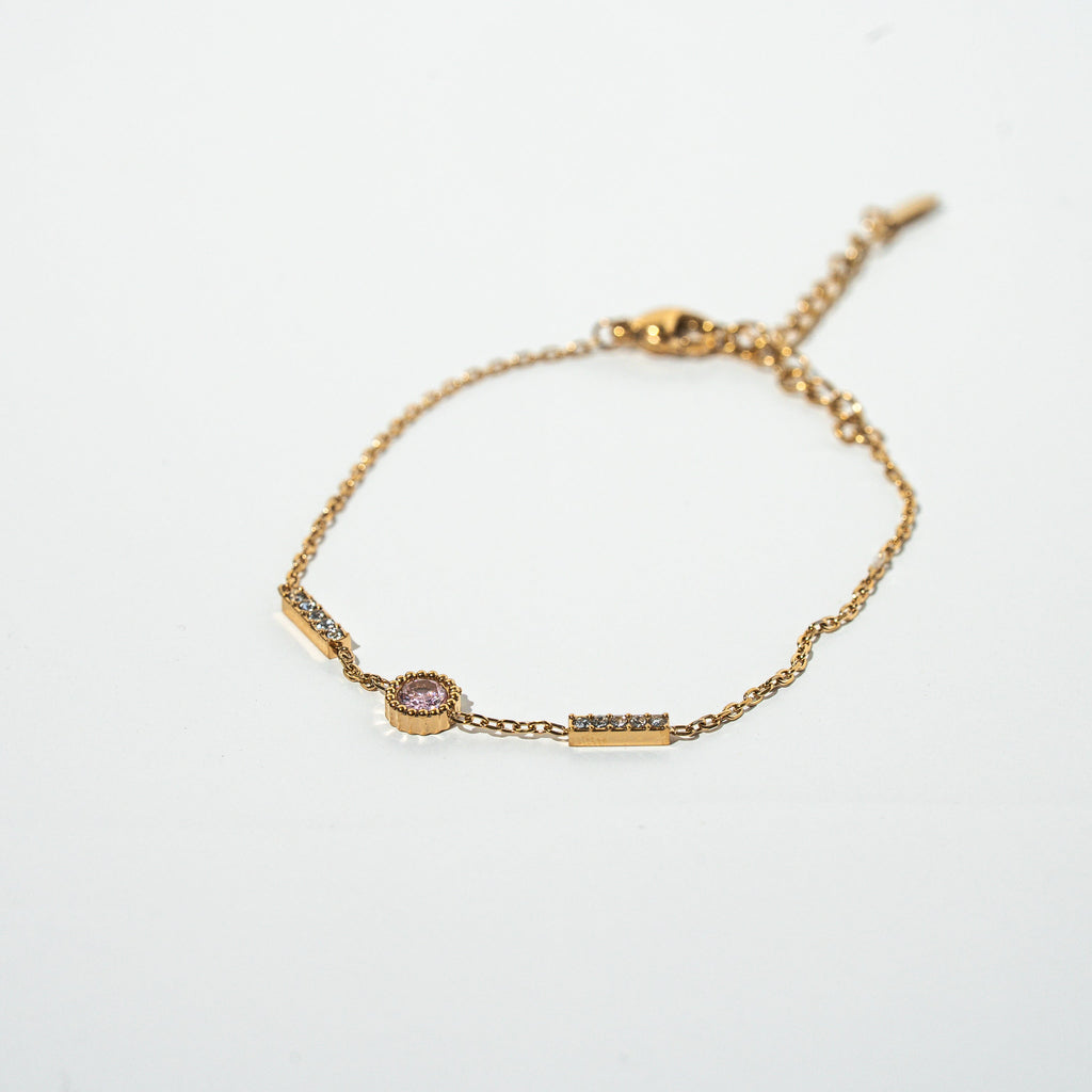 Gold bracelet with a small pink gemstone on a light gray background. Harma Jewelry gold plated I Am Healing PINK Zirconia Bracelet
