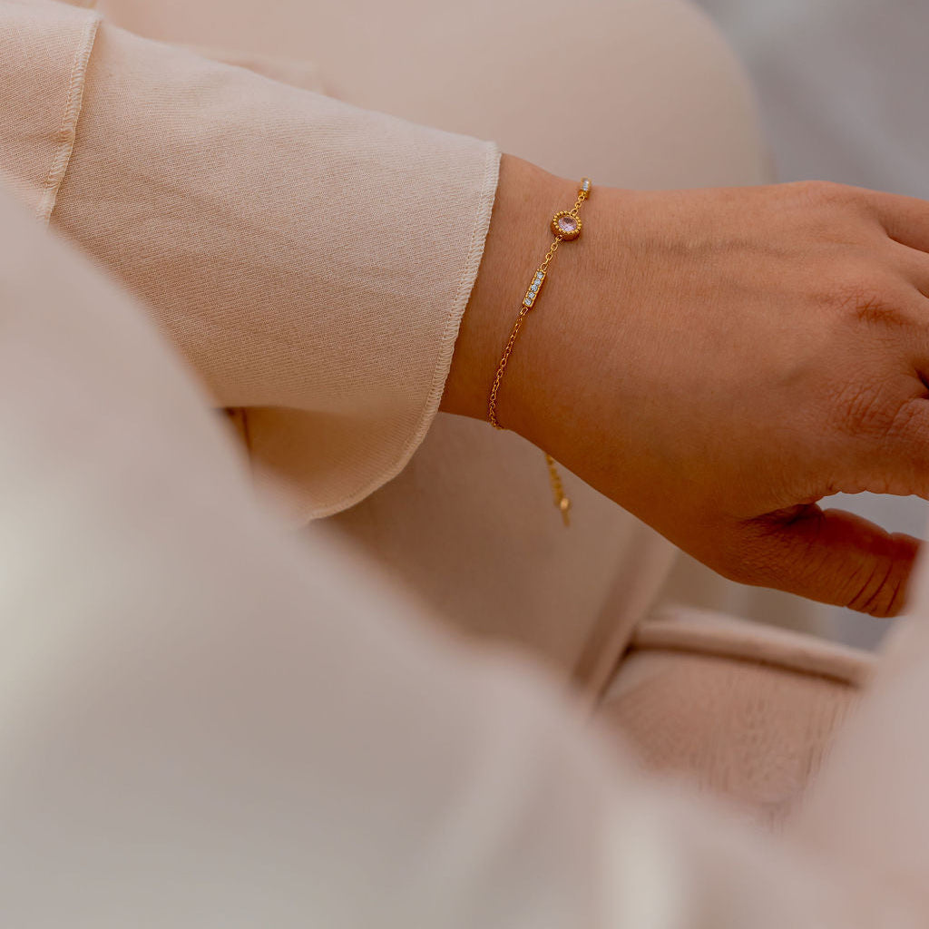 Close-up of a hand wearing a gold bracelet on a blurred background. Harma Jewelry gold plated I Am Healing PINK Zirconia Bracelet