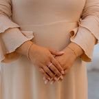 Person wearing a beige dress with ruffled sleeves, holding hands together. Harma Jewelry gold plated I Am Healing PINK Zirconia Bracelet
