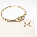 Gold bracelet with decorative elements on a white card with a butterfly design. Harma Luminous Noor Lantern Bracelet