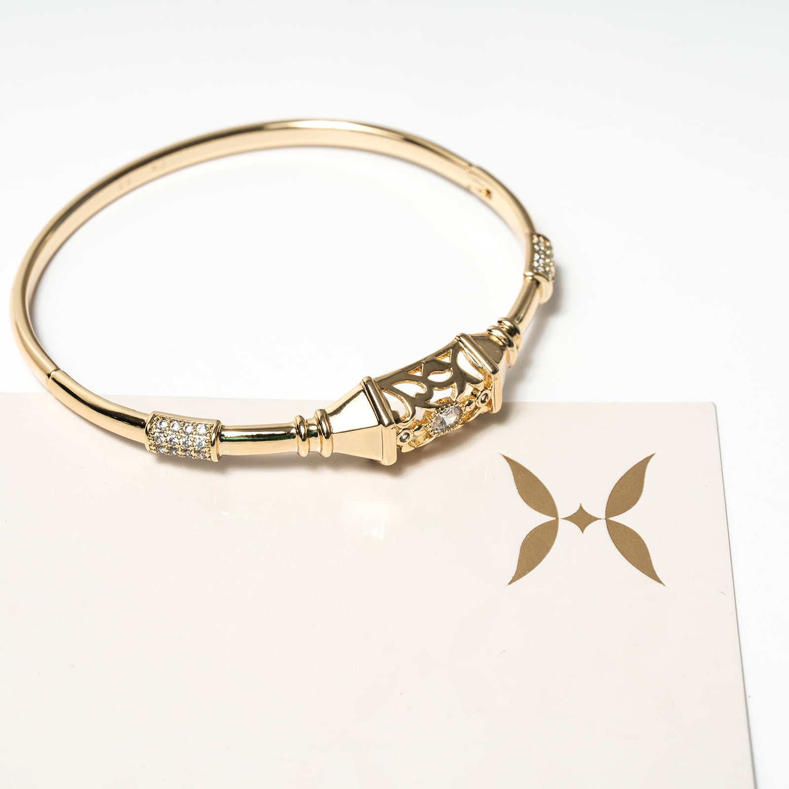 Gold bracelet with decorative elements on a white card with a butterfly design. Harma Luminous Noor Lantern Bracelet