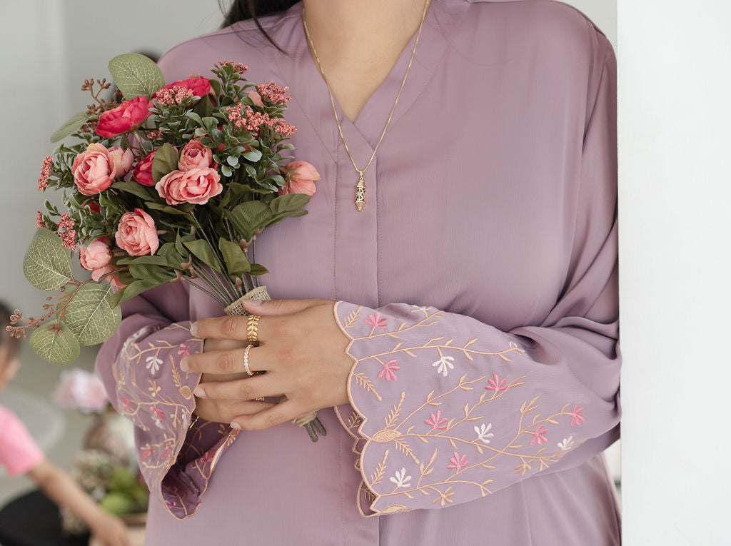 Person holding a bouquet of flowers wearing a purple dress with floral embroidery. Harma Luminous Noor Lantern Necklace Set