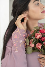 Woman wearing a lavender dress with floral embroidery, holding a bouquet of flowers. Harma Luminous Noor Lantern Necklace Set