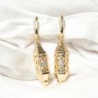 Gold earrings with diamond accents on a white satin background. Harma Luminous Noor Lantern Necklace Set
