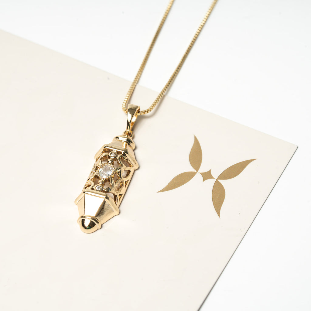 Gold necklace with a pendant on a white card with a brand logo. Harma Luminous Noor Lantern Necklace Set