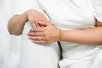 Close-up of a person's hands holding each other, wearing gold rings and bracelets on a white background.