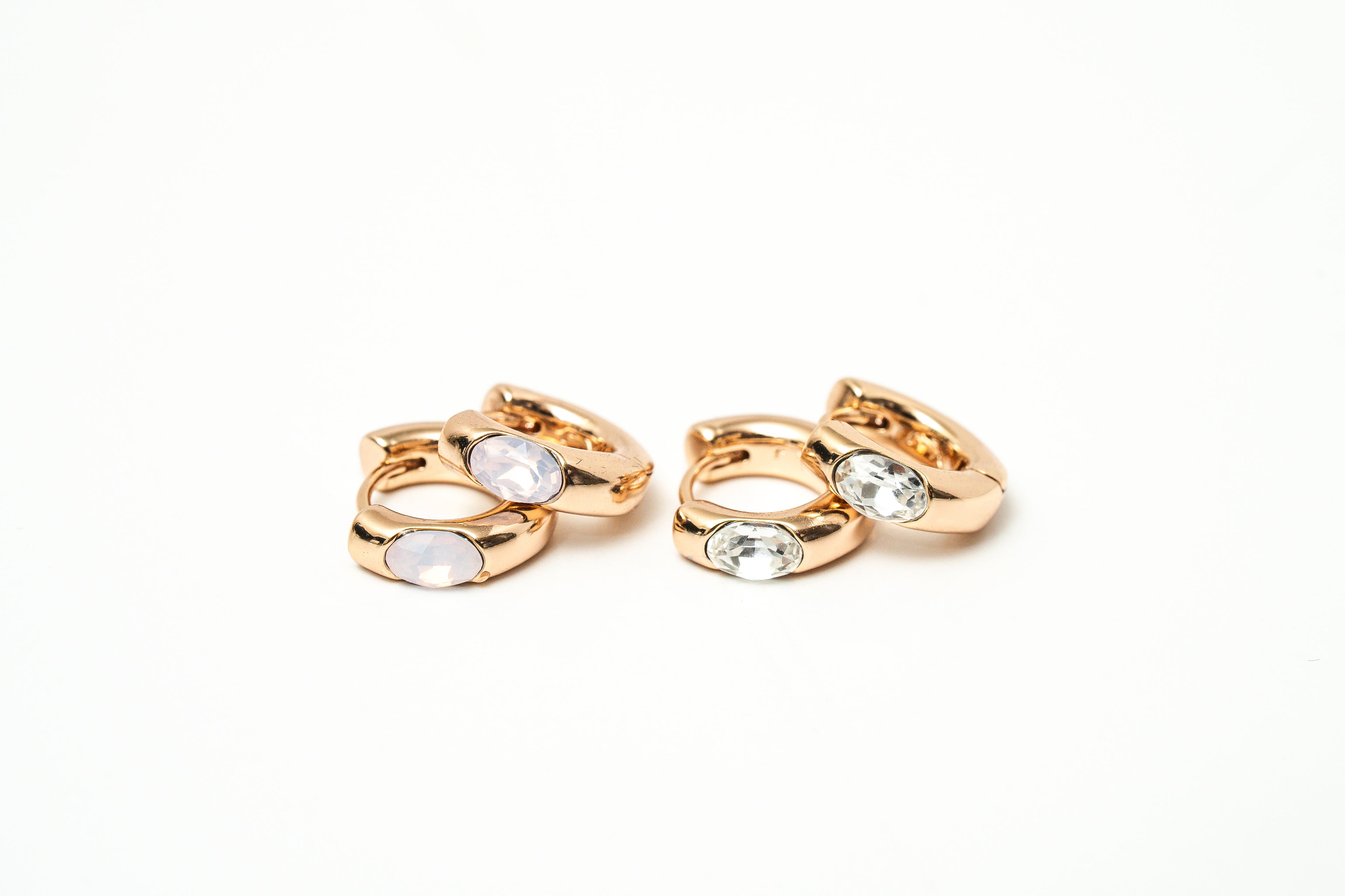 Pair of rose gold hoop earrings with clear gemstones on a white background