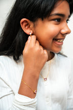 Young girl wearing a gold earring and bracelet, smiling.