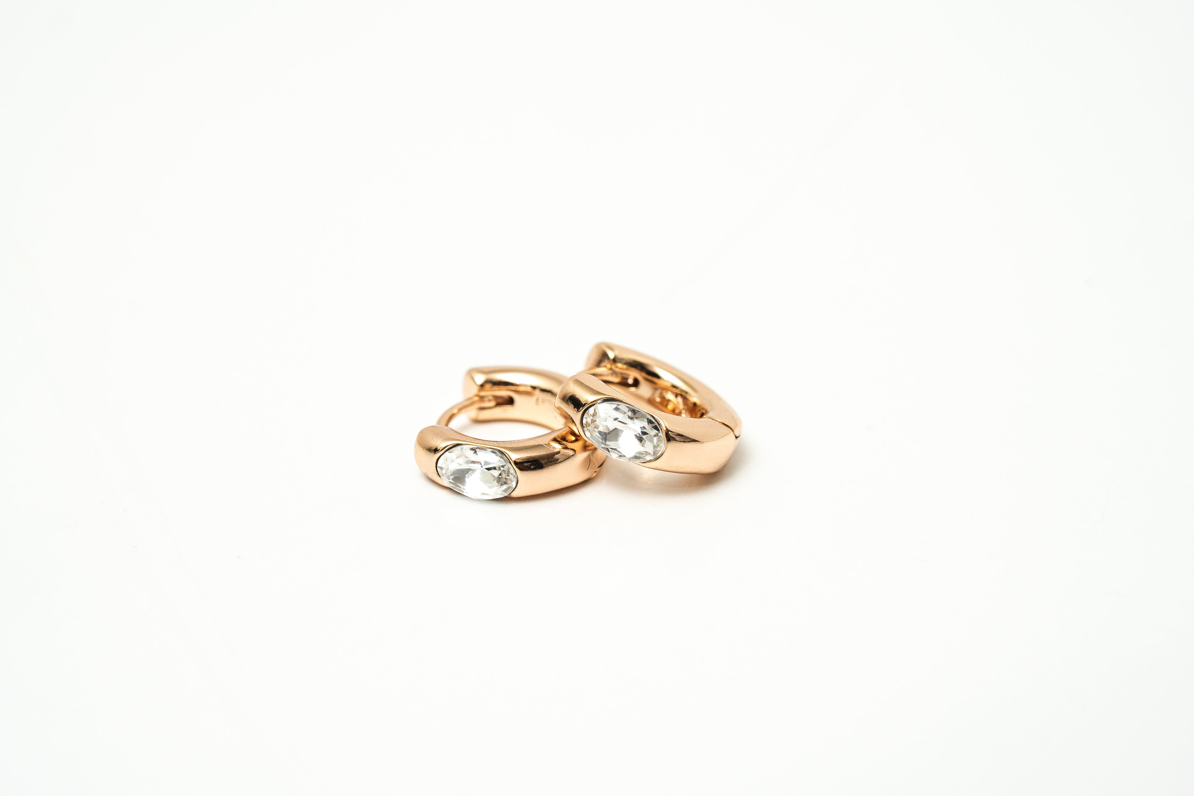 Pair of rose gold hoop earrings with clear gemstones on a white background
