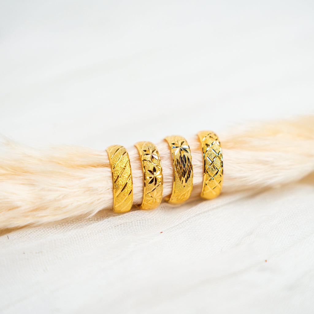 Three gold rings stacked on a piece of light wood. Timeless Bands – 24K Gold-Plated Adjustable Rings
