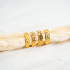 Three gold rings stacked on a piece of light wood. Timeless Bands – 24K Gold-Plated Adjustable Rings