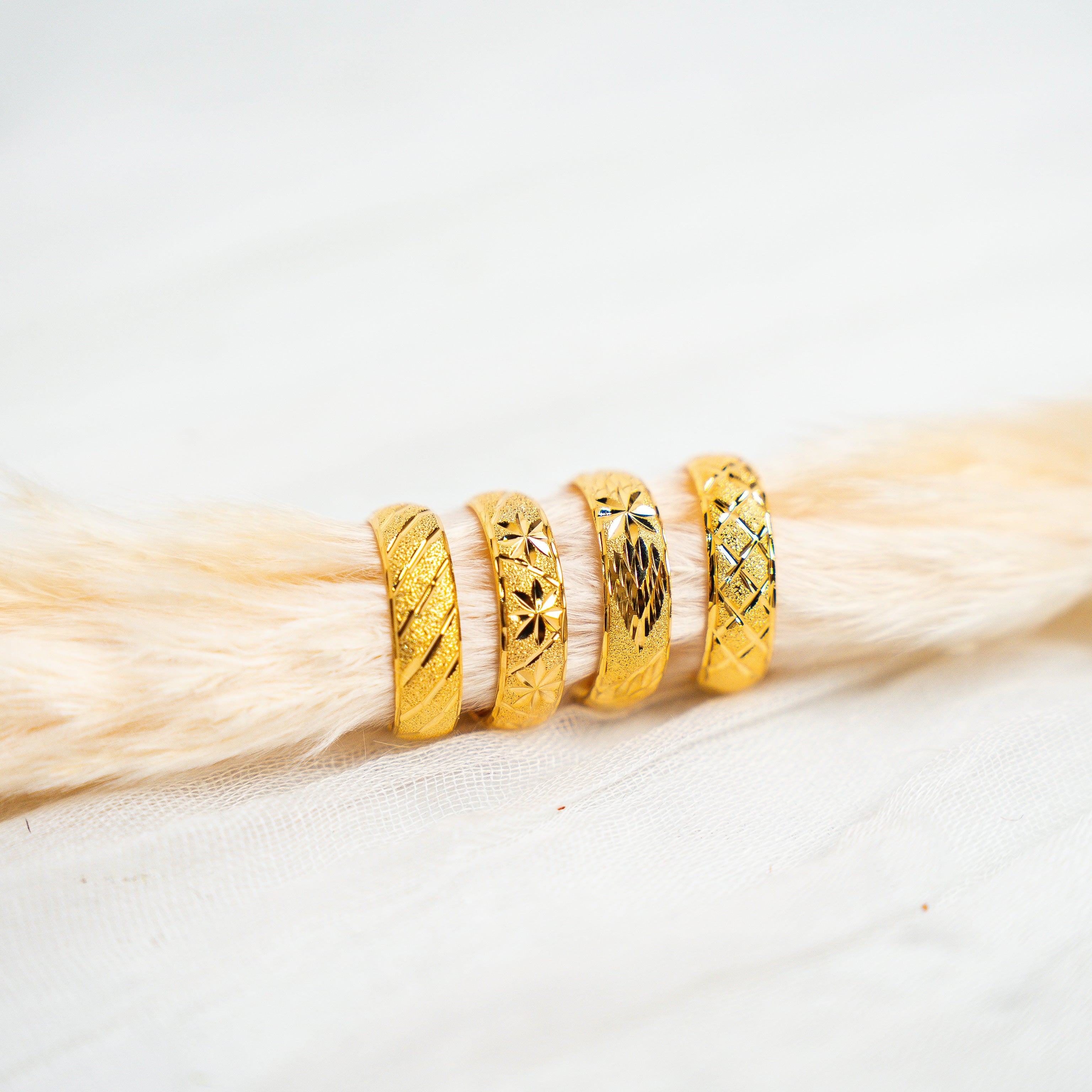 Three gold rings stacked on a piece of light wood. Timeless Bands – 24K Gold-Plated Adjustable Rings